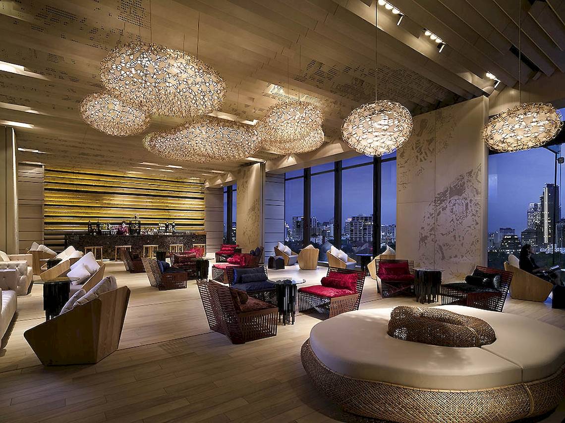 Innenansicht des SO/ Bangkok Hotel-Lounges mit großen Kronleuchtern, Möbeln und Blick auf die Stadt.