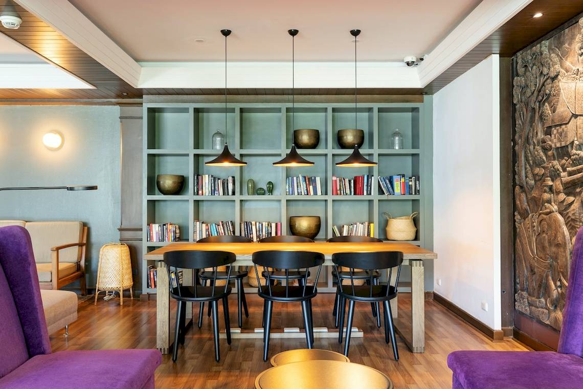 Essbereich im Sunprime Kamala Beach Hotel mit einem runden Tisch und Stühlen, Regalen mit Büchern und Dekoration.