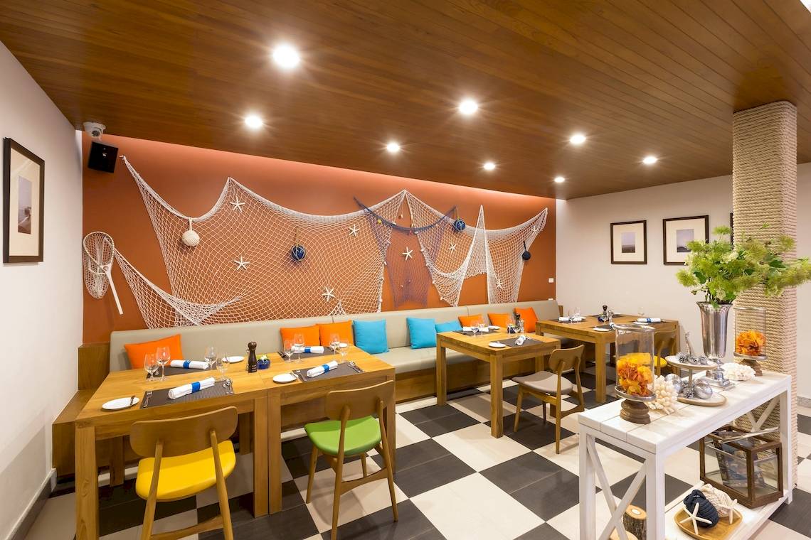 Innenansicht des Restaurants im X10 Khaolak Resort mit blauen Kissen, Holztischen und maritimen Dekorationen.