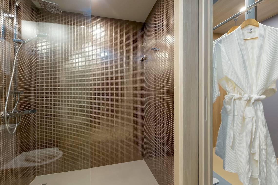 Dusche im X10 Khaolak Resort mit weißen Bademantel, der an einem Kleiderbügel hängt.