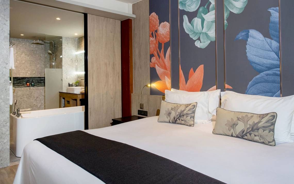 Hotelzimmer im La Flora Khao Lak mit Bett, Kissen, Badewanne und Badezimmerspiegel.