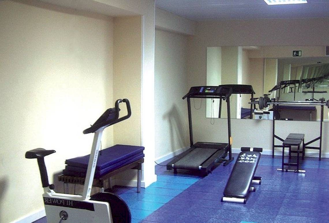 Fitnessraum im Argos Hotel mit Geräten und Spiegeln.