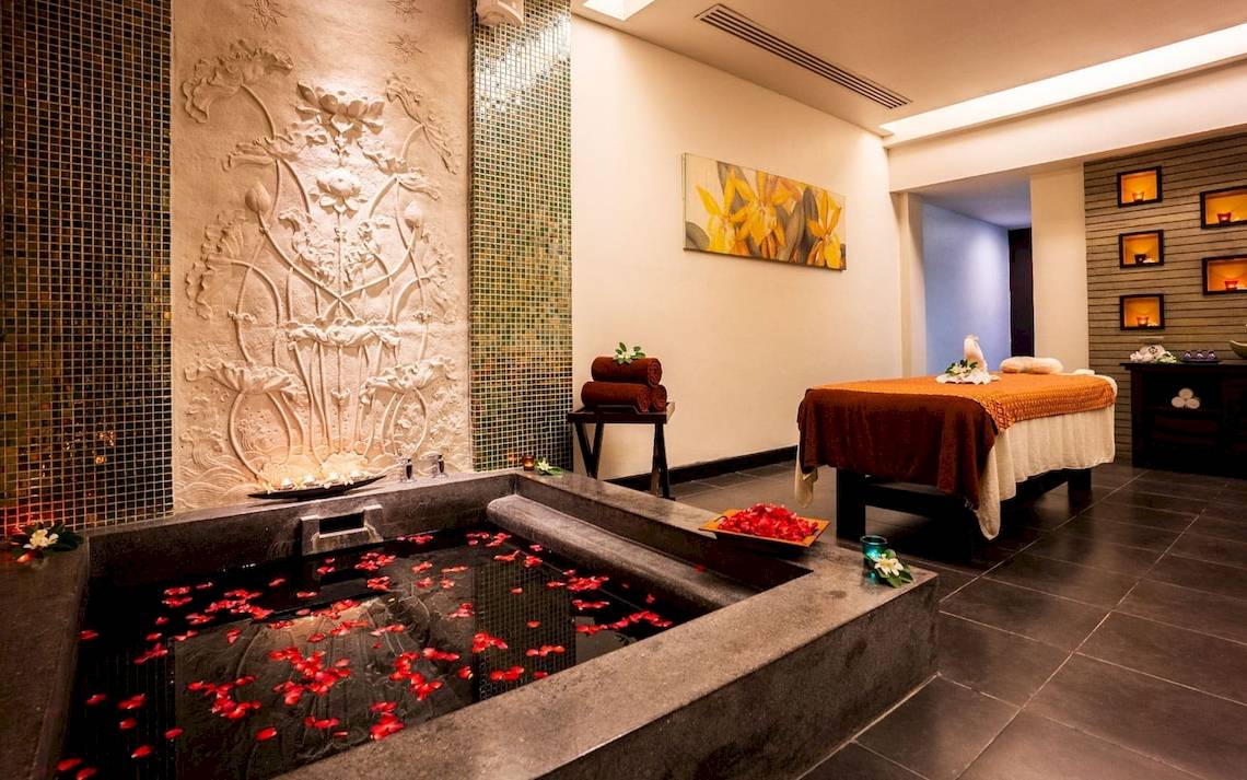 Spa-Behandlungsraum im La Flora Khao Lak mit einem großen Becken, Rosenblättern, Massagetisch und Wandverzierungen.
