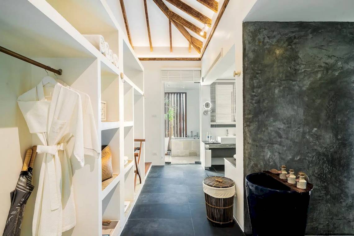 Innenansicht der TreeHouse Villas Koh Yao mit weißen Regalen, schwarzen Fliesen und einem weißen Bademantel