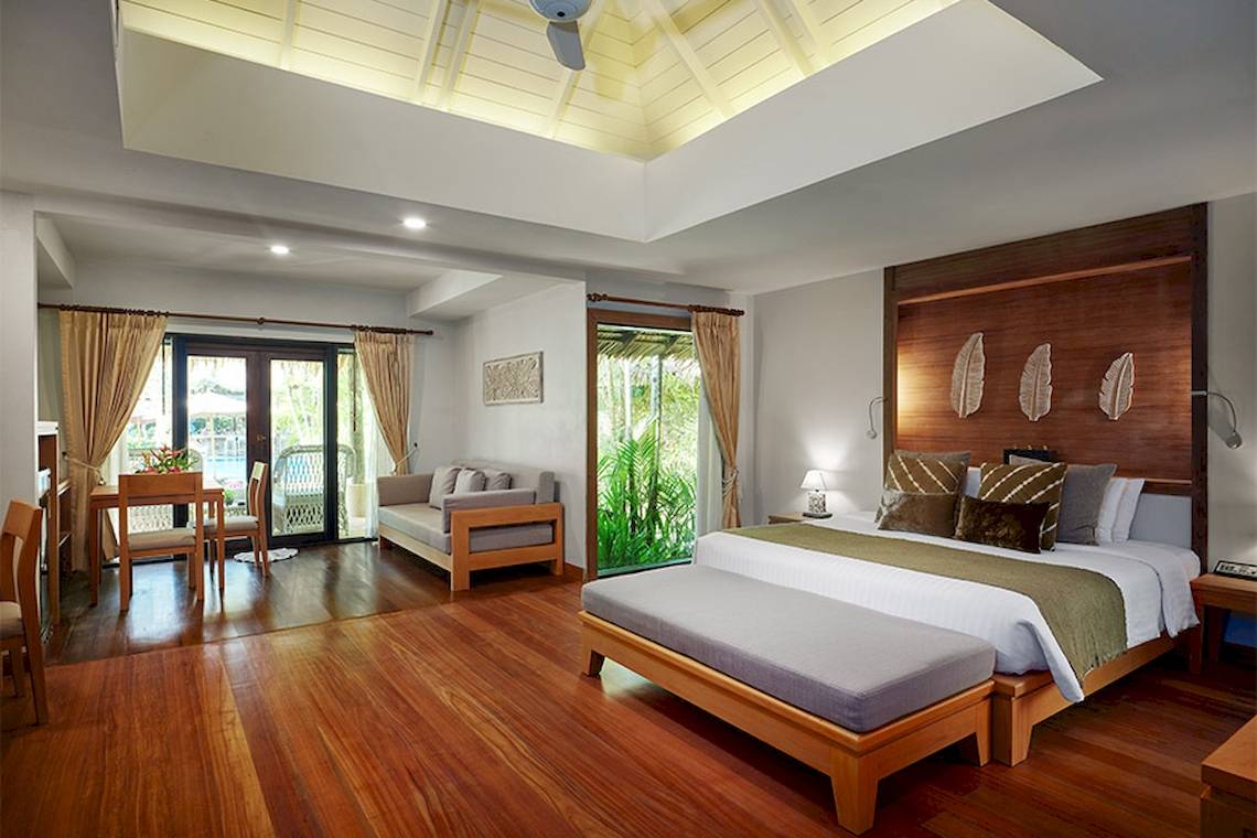 Innenansicht eines Zimmers im Khaolak Paradise Resort mit Holzboden, Bett, Couch, Tisch und Fenstern.