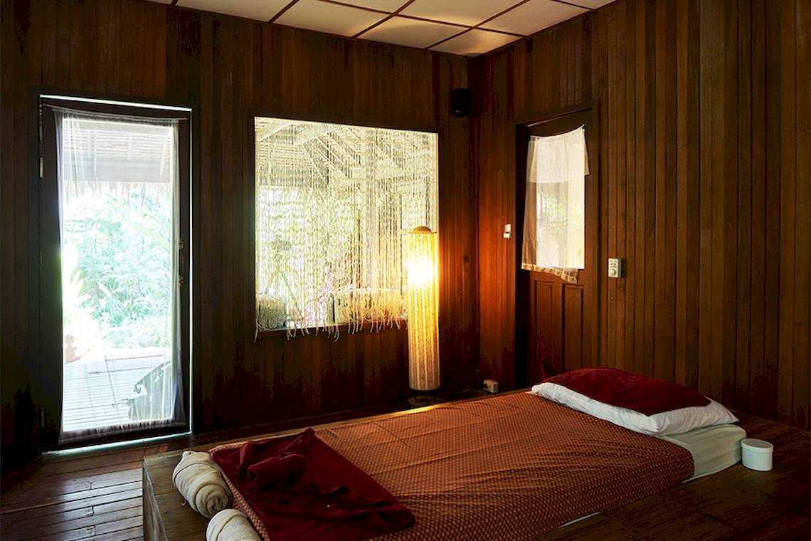 Ein Bett in einem Holzraum des Khaolak Paradise Resort mit einem roten Laken und Kissen.