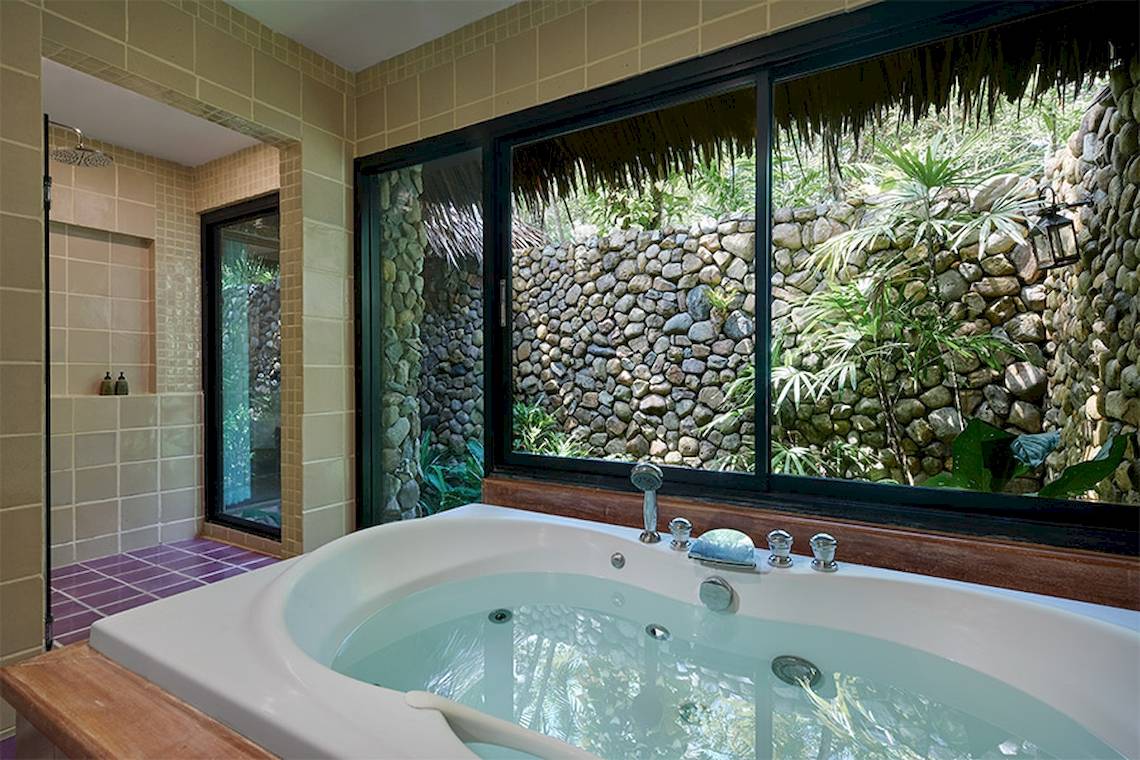 Badezimmer im Khaolak Paradise Resort mit Badewanne und Fenster mit Blick auf einen steinernen Garten.
