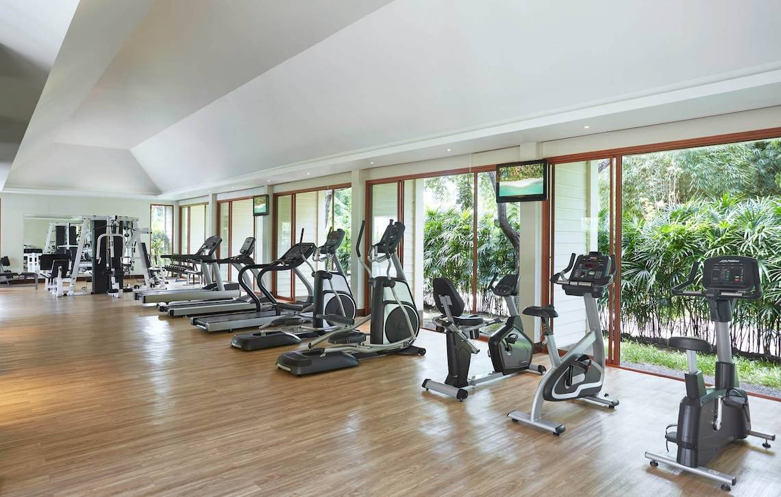 Fitnesscenter im Santiburi Koh Samui Hotel mit vielen Trainingsgeräten und Panoramafenstern.