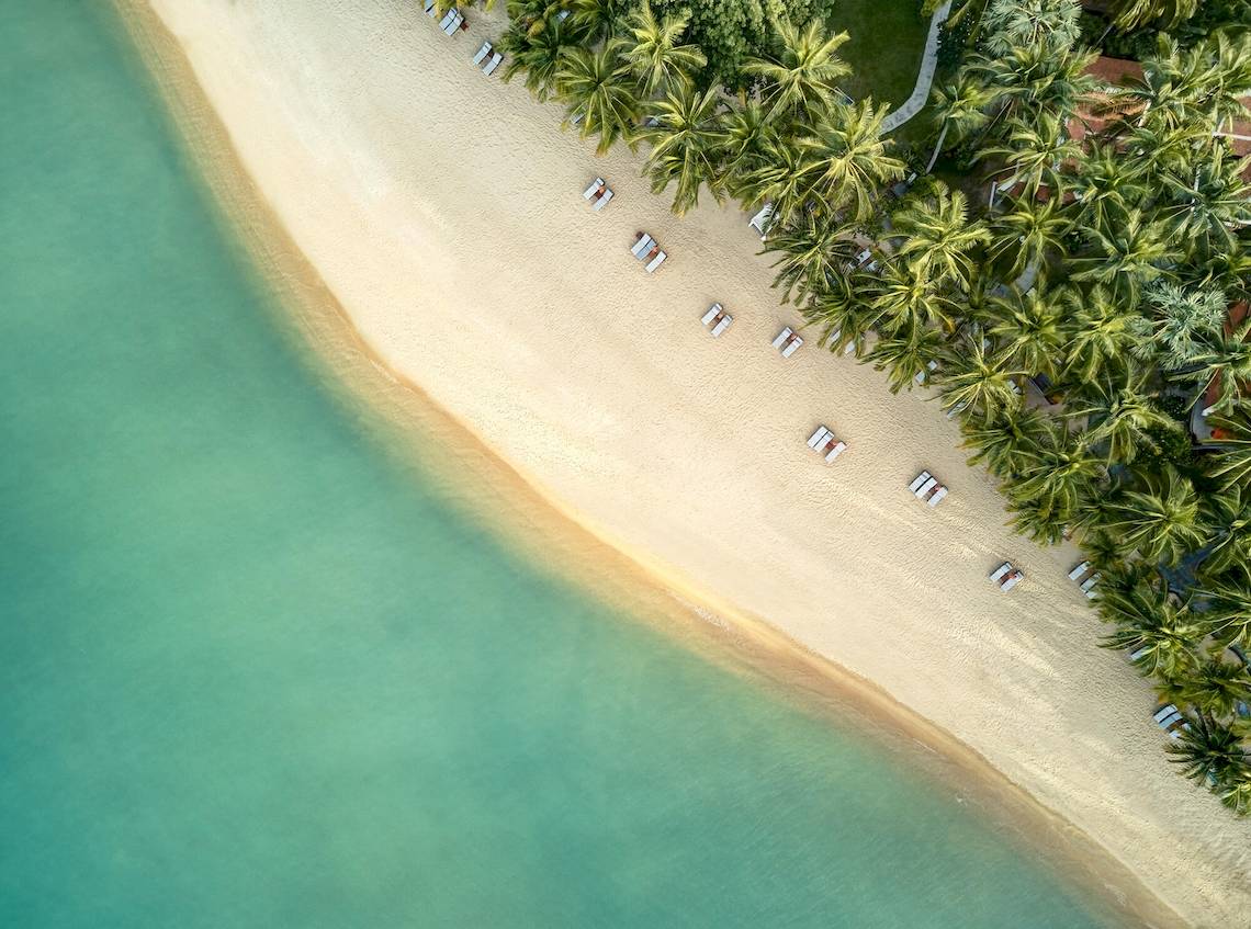 Luftaufnahme des Santiburi Koh Samui Strandes mit weißen Sonnenliegen und Palmen