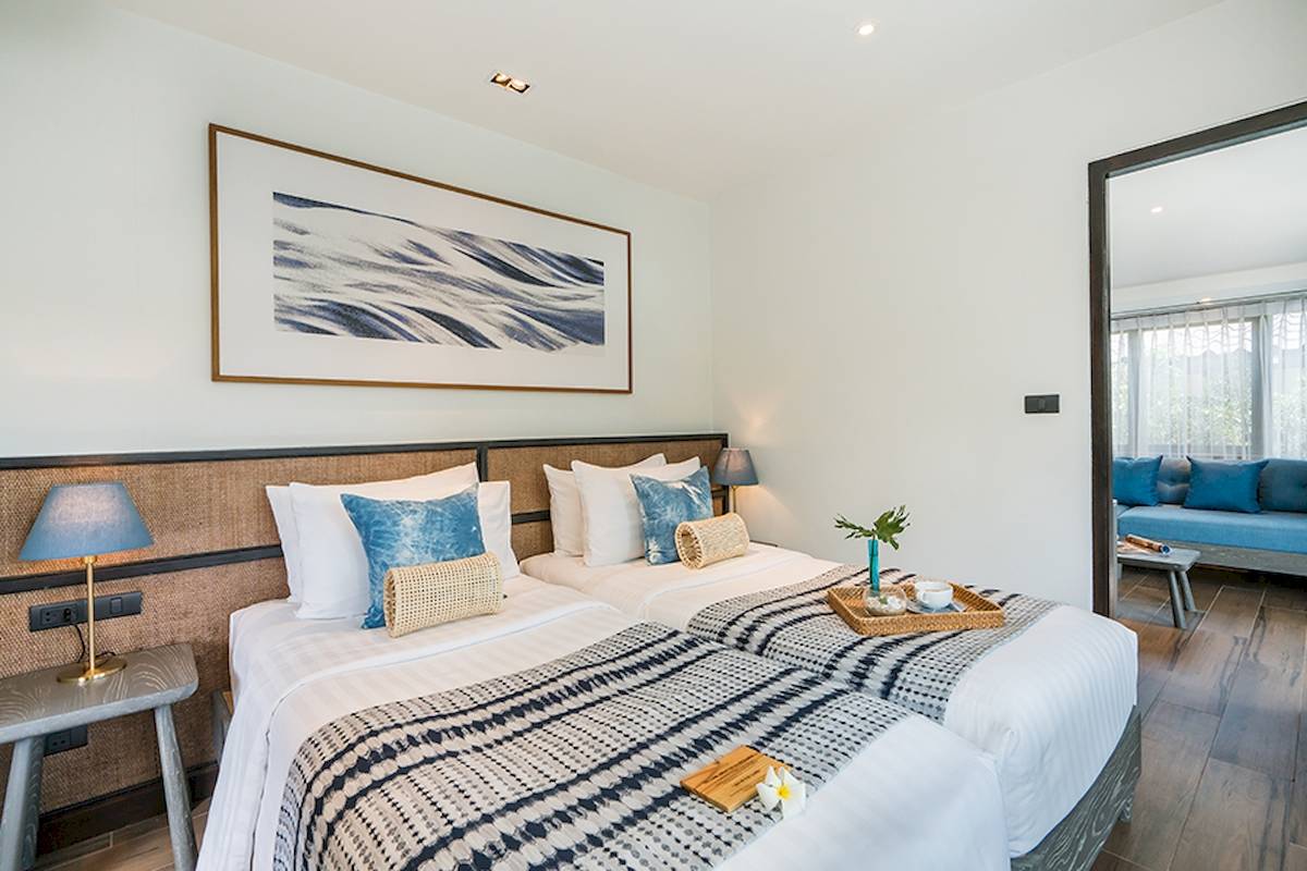 Doppelbettzimmer im Peace Resort mit moderner Einrichtung, weiße Wände, blaue Kissen und ein gerahmtes Bild.