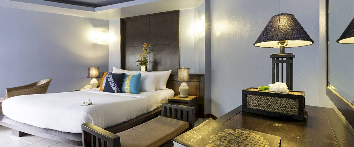Doppelbett-Zimmer im Peace Laguna Resort & Spa mit weißen Bettlaken, Kissen und Nachttischen mit Lampen.