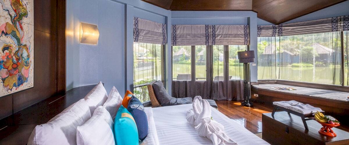Hotelzimmer im Peace Laguna Resort & Spa mit blauen Wänden, Fenstern, einem Bett, Kissen und einem Ausblick auf einen See.
