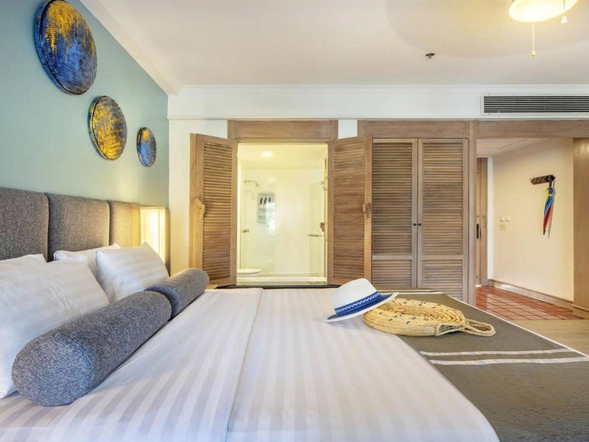 Ein modernes Hotelzimmer mit einem großen Bett, mehreren Kissen und Accessoires wie einem Hut und einer Tasche.
