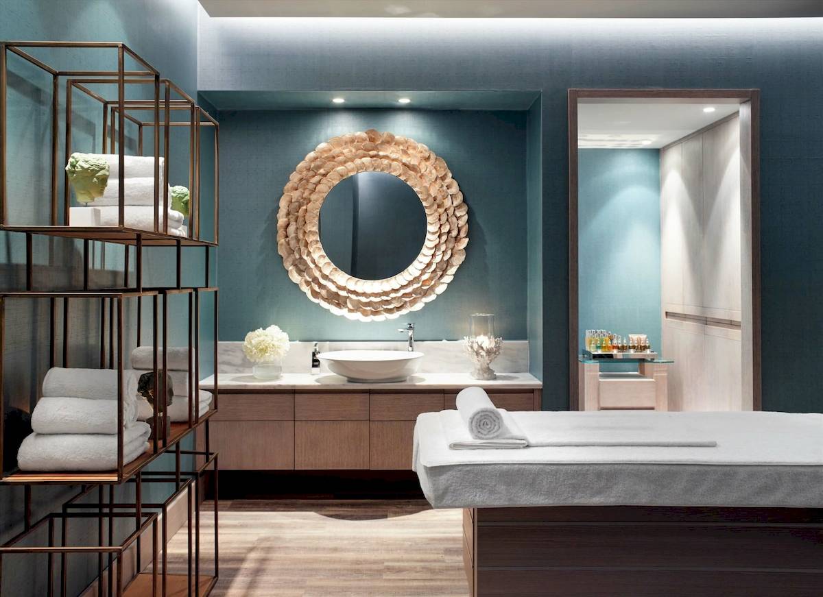 Wellnessbereich im Ikos Aria Hotel mit runden Spiegel, weißen Handtüchern und einer Tischlampe.
