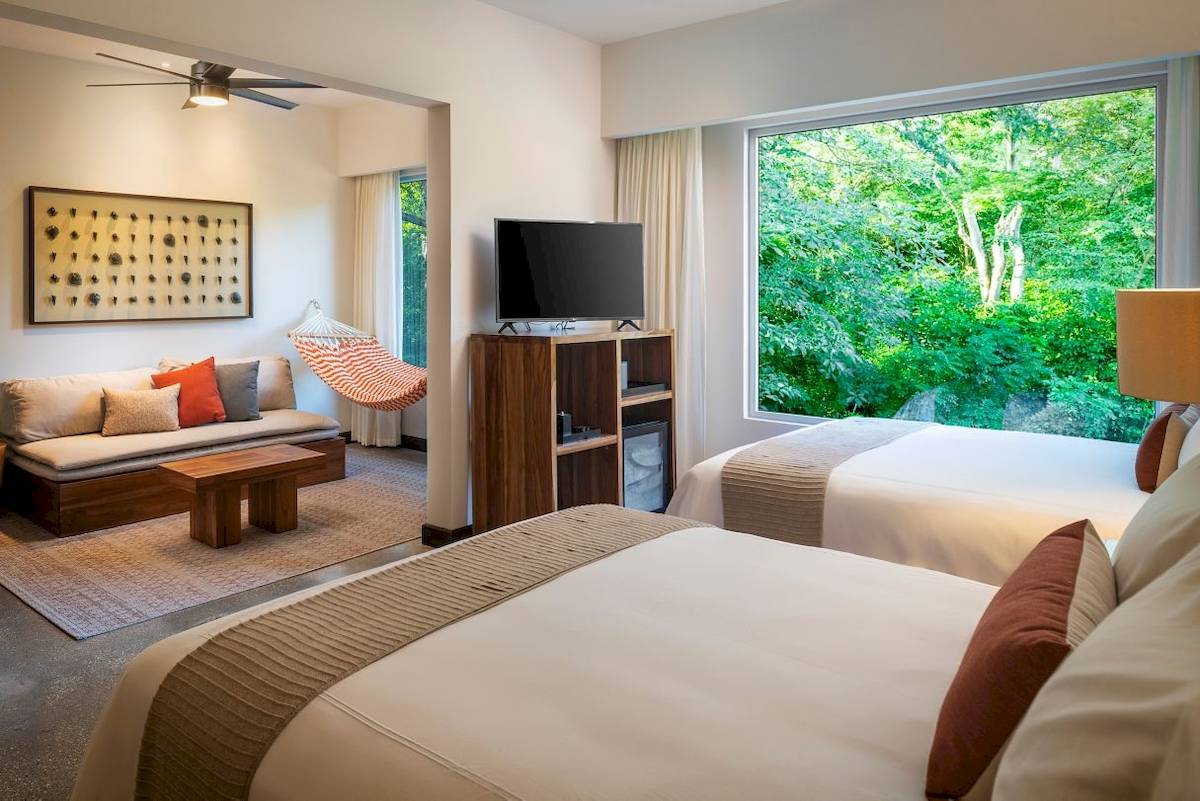 Hotelzimmer im El Mangroove Autograph Collection mit zwei Betten, Fernseher, Sofa und Aussicht auf den Garten.