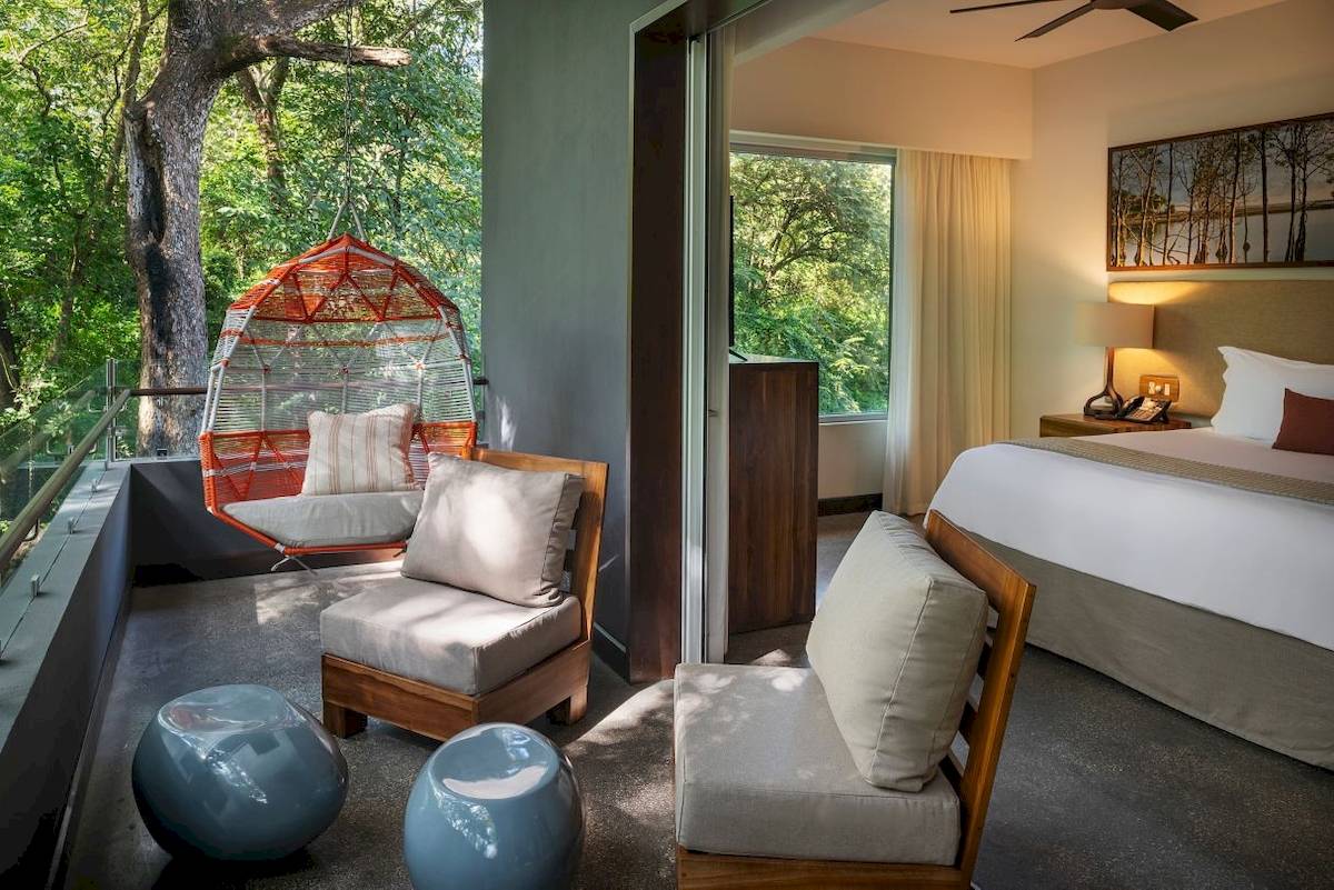 Zimmer mit Balkon im El Mangroove, Autograph Collection Hotel, mit Hängestuhl, Betten und Ausblick auf Bäume.