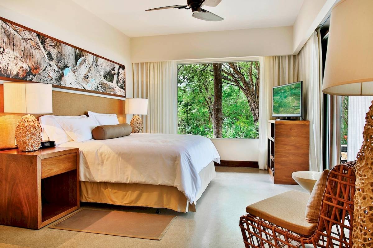 Schlafzimmer im El Mangroove, Autograph Collection mit großem Bett, Fenstern und Ausblick auf Bäume.