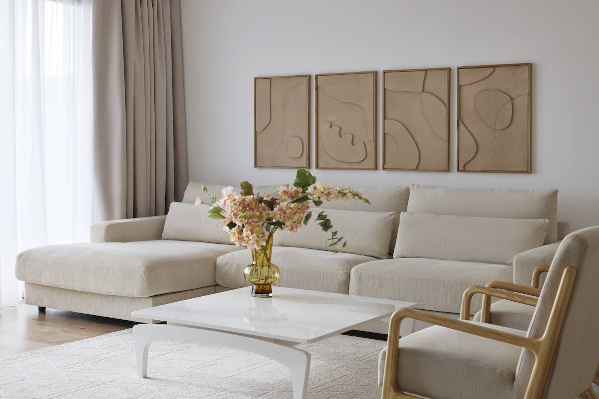 Wohnzimmer im Melia Durres Hotel in Albanien mit beigefarbener Couch, Blumenvase und drei Wandbildern.