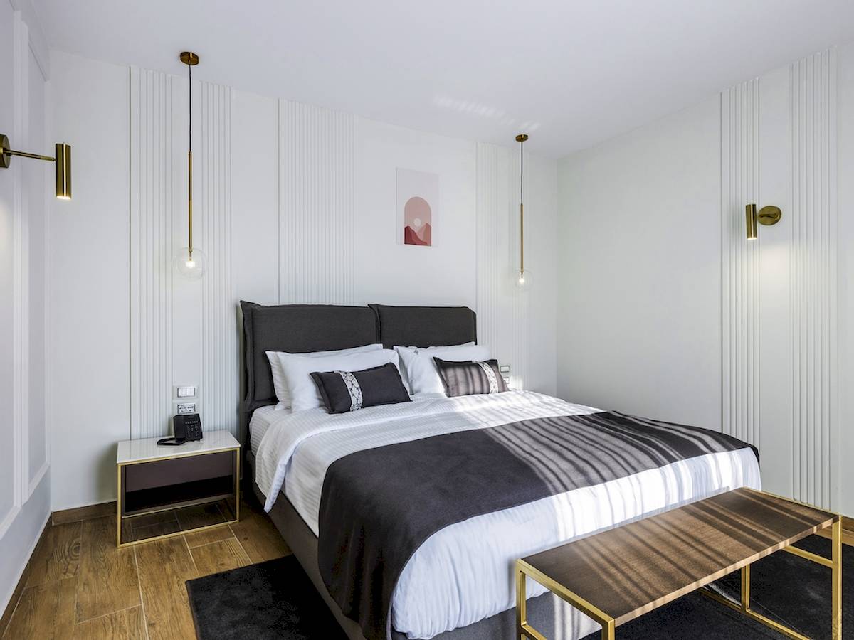 Schlafzimmer im Mövenpick Hotel Lalez Durres mit weißem Bett, goldfarbenen Lampen und modernem Design.