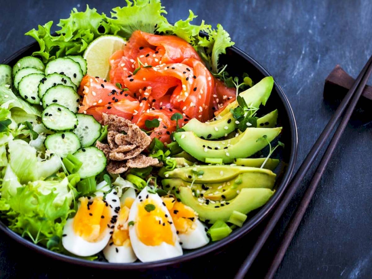 Ein Salat mit Salatblättern, Gurkenscheiben, Lachs, Avocado und Eiern in einer Schüssel.