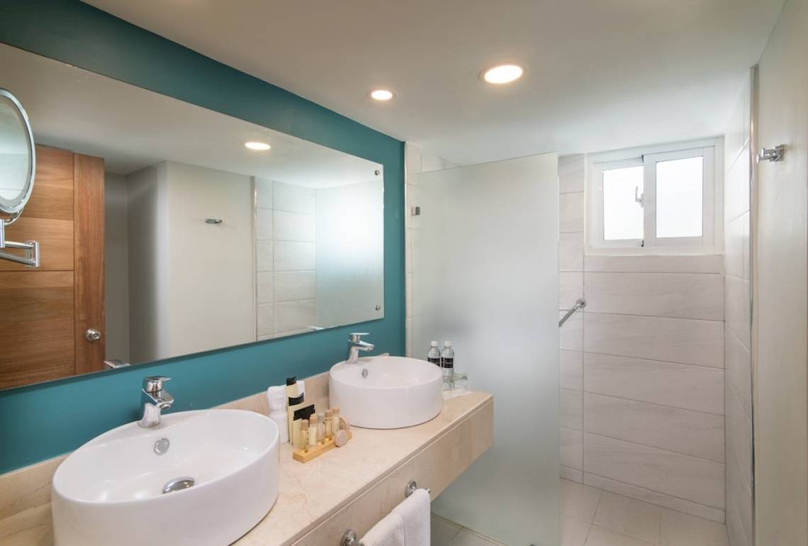 Badezimmer im Emotions By Hodelpa Hotel mit zwei Waschbecken, Spiegel und Duschkabine.