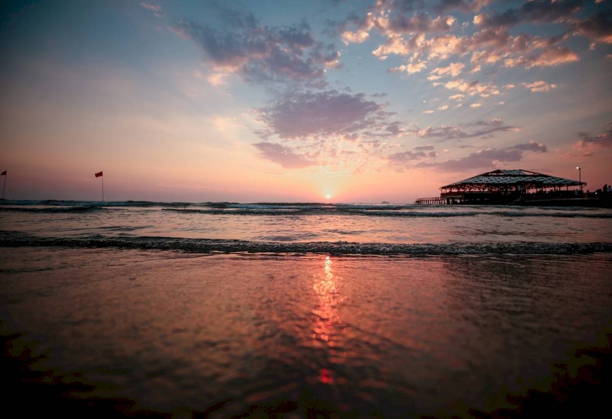 Sonnenuntergang am Strand mit einem Pavillon im Hintergrund und roten Fahnen im Wasser