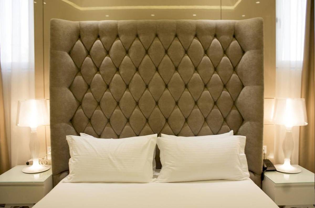 Hotelbett mit gepolstertem Kopfteil, weißen Kissen und Nachttischen mit Lampen.