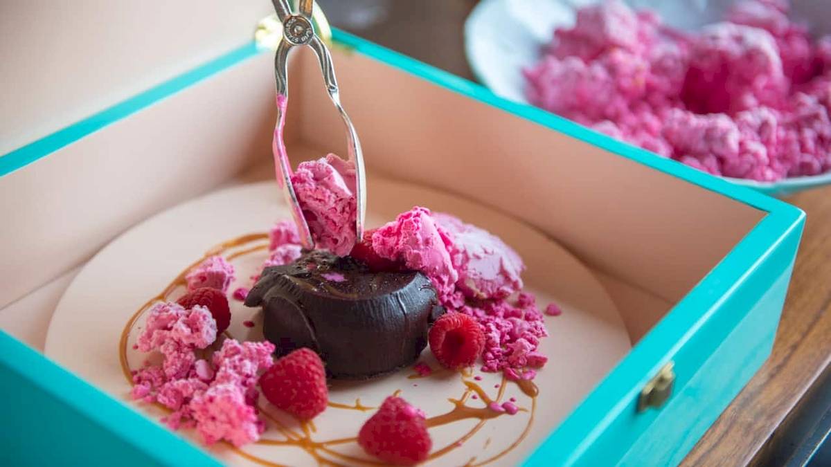 Ein Schokoladen-Dessert in einer blauen Schachtel mit rosa Eis und Himbeeren.
