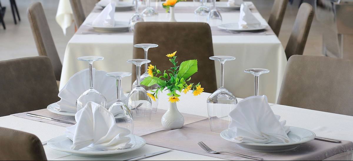 Ein Tisch im Dyrrah Hotel ist gedeckt mit Tellern, Gläsern und einem Blumenstrauß in einer Vase.