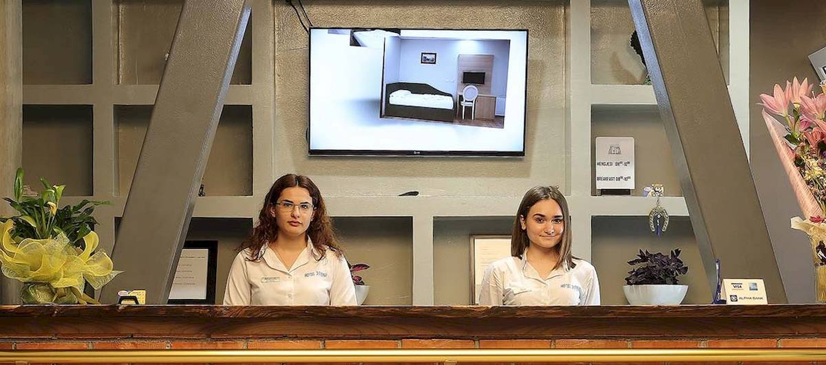 Zwei Frauen an der Rezeption des Dyrrah Hotels, davor eine Anzeige auf einem Monitor.