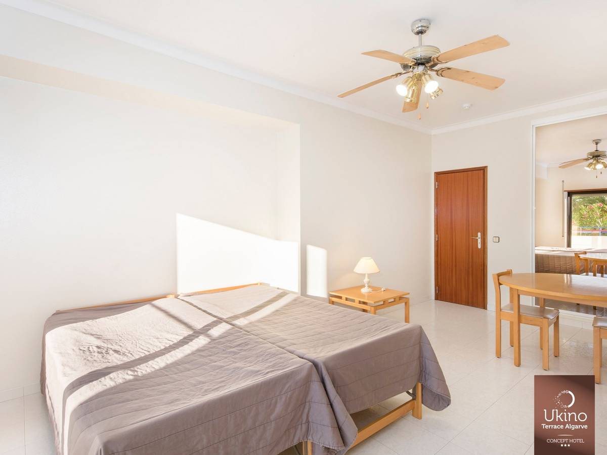 Innenansicht eines Schlafzimmers im Ukino Terrace Algarve Hotel mit zwei Betten, Nachttisch, Lampe, Esstisch und Stühlen.