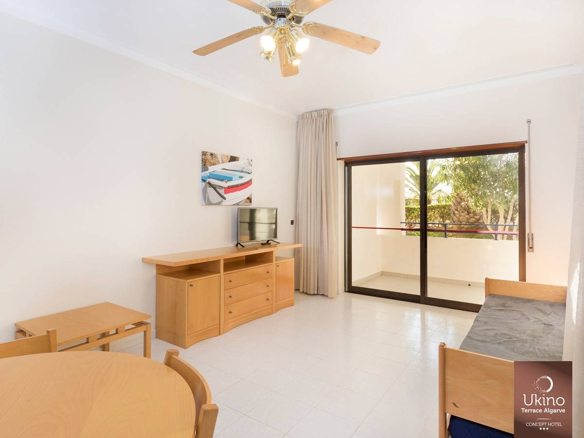 Innenraum des Ukino Terrace Algarve Hotels mit Wohnzimmer, Fernseher, Tisch und Stühlen.