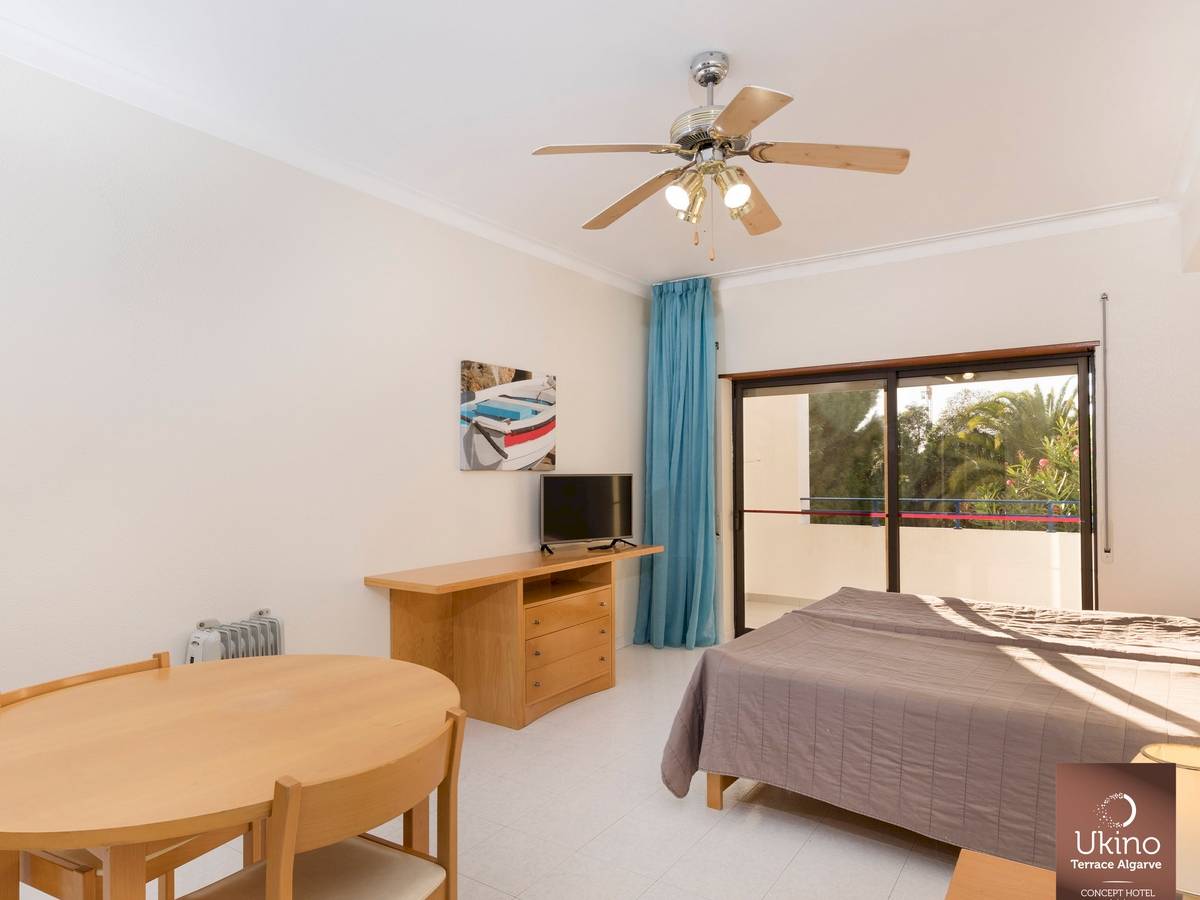 Innenansicht eines Zimmers im Ukino Terrace Algarve Hotel mit Bett, Tisch, Fernseher und Balkon.