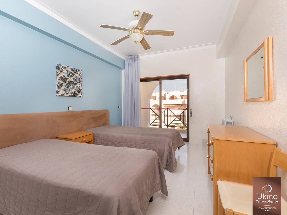 Schlafzimmer im Ukino Terrace Algarve Hotel mit zwei Betten, Deckenventilator und Zugang zur Terrasse.