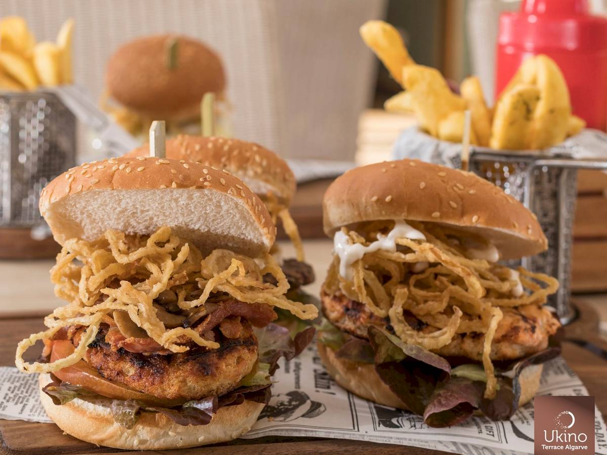 Hühnchenburger mit gebratenen Zwiebeln und Pommes frites auf einer Holzplatte.