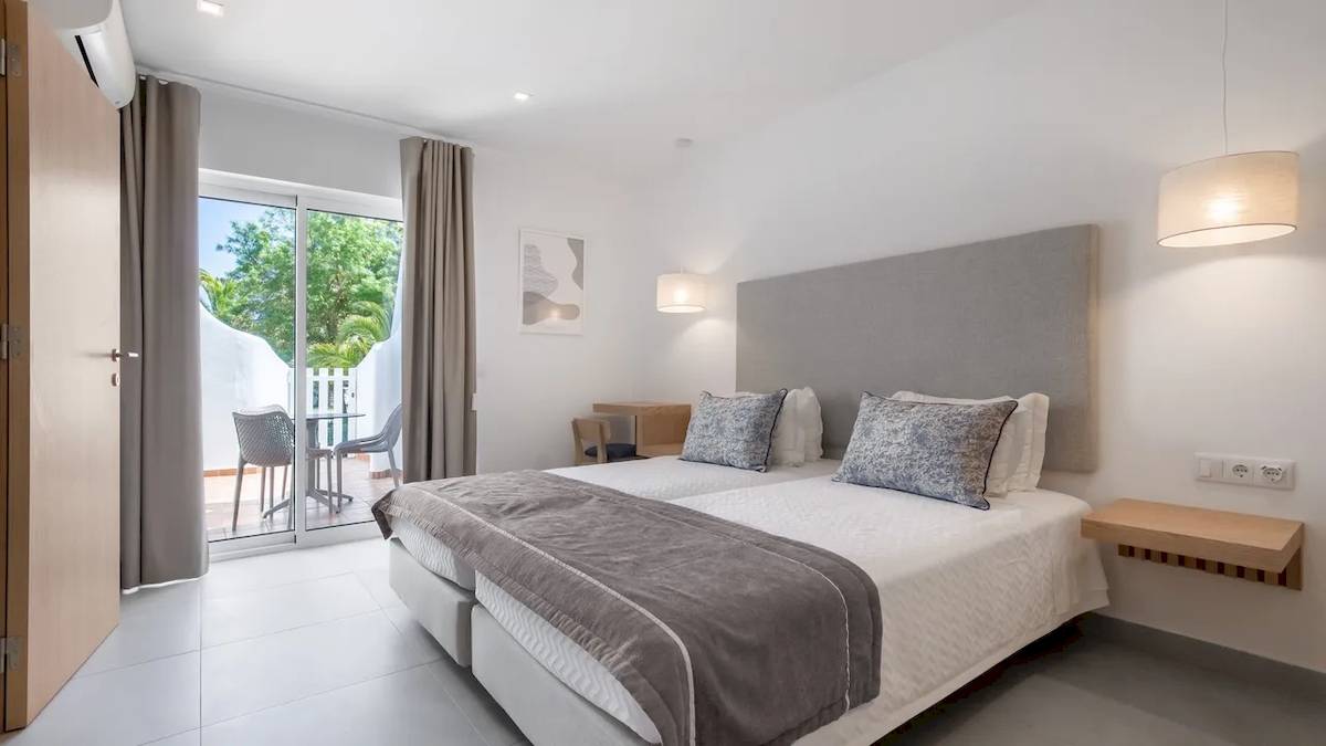 Doppelbett-Zimmer mit Balkon im Ancora Park Hotel, modernes Design mit weißer Wand, Glastür und grüner Vorhang.