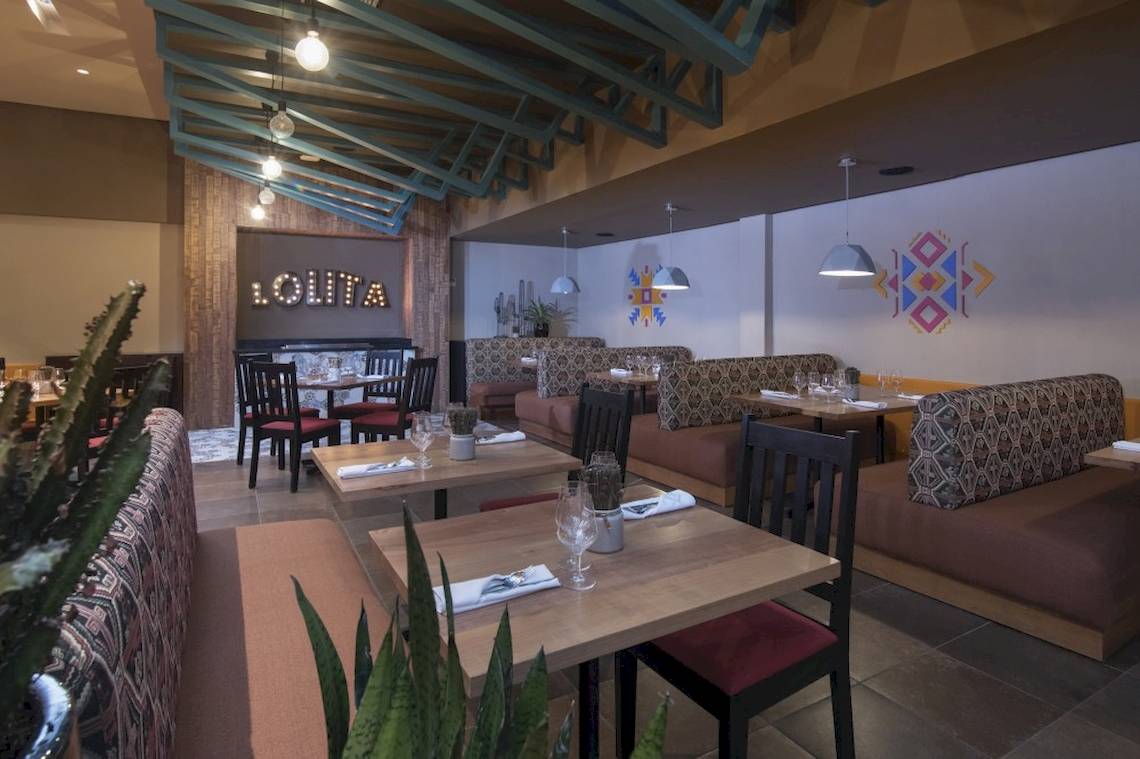 Innenansicht des Restaurants im Emotions By Hodelpa Hotel in Puerto Plata mit gepolsterten Sitzen und Tischen.