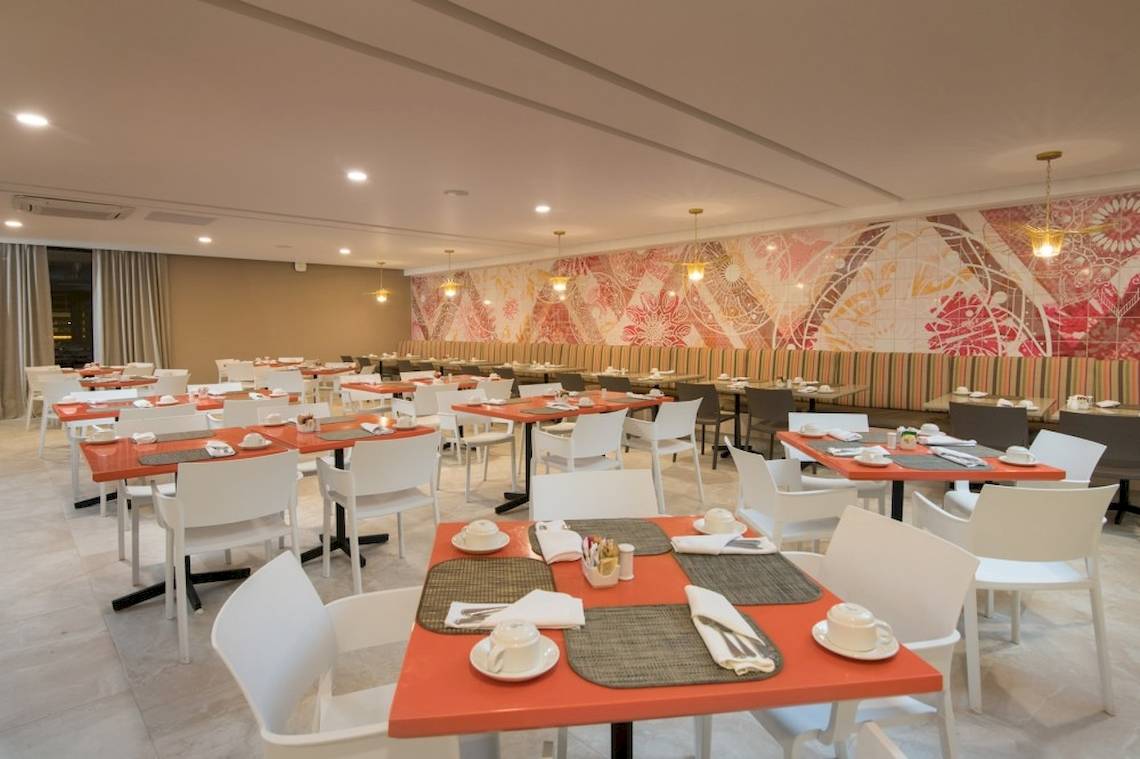 Frühstücksraum des Emotions By Hodelpa Hotels mit orangefarbenen Tischen und weißen Stühlen.