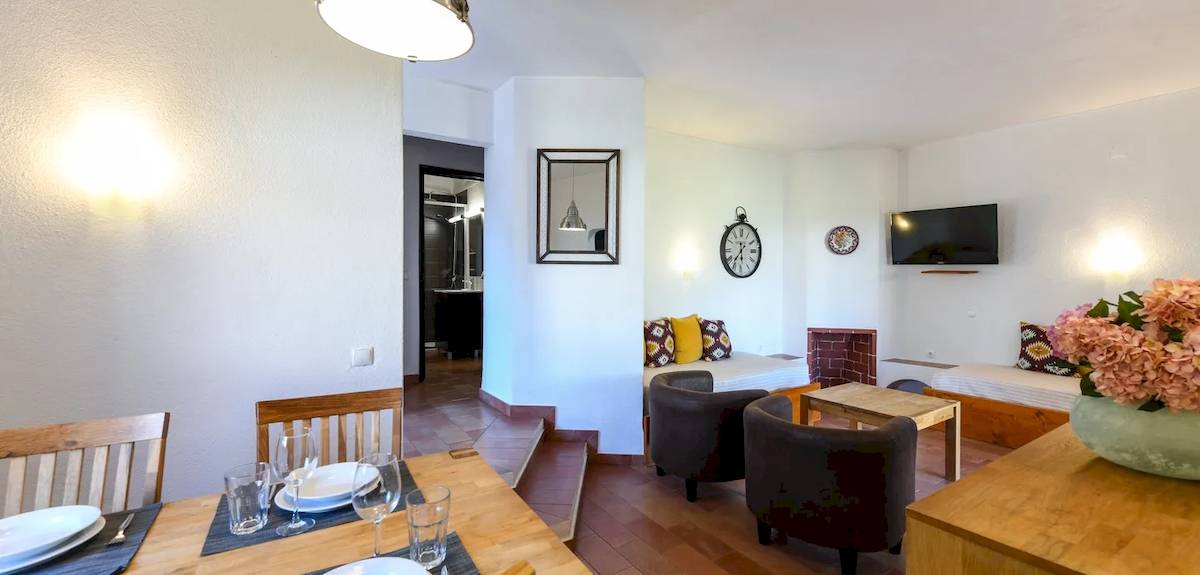 Inneneinrichtung des Pedras da Rainha Resorts mit Esstisch, Sesseln, Fernseher und Blumenvase.