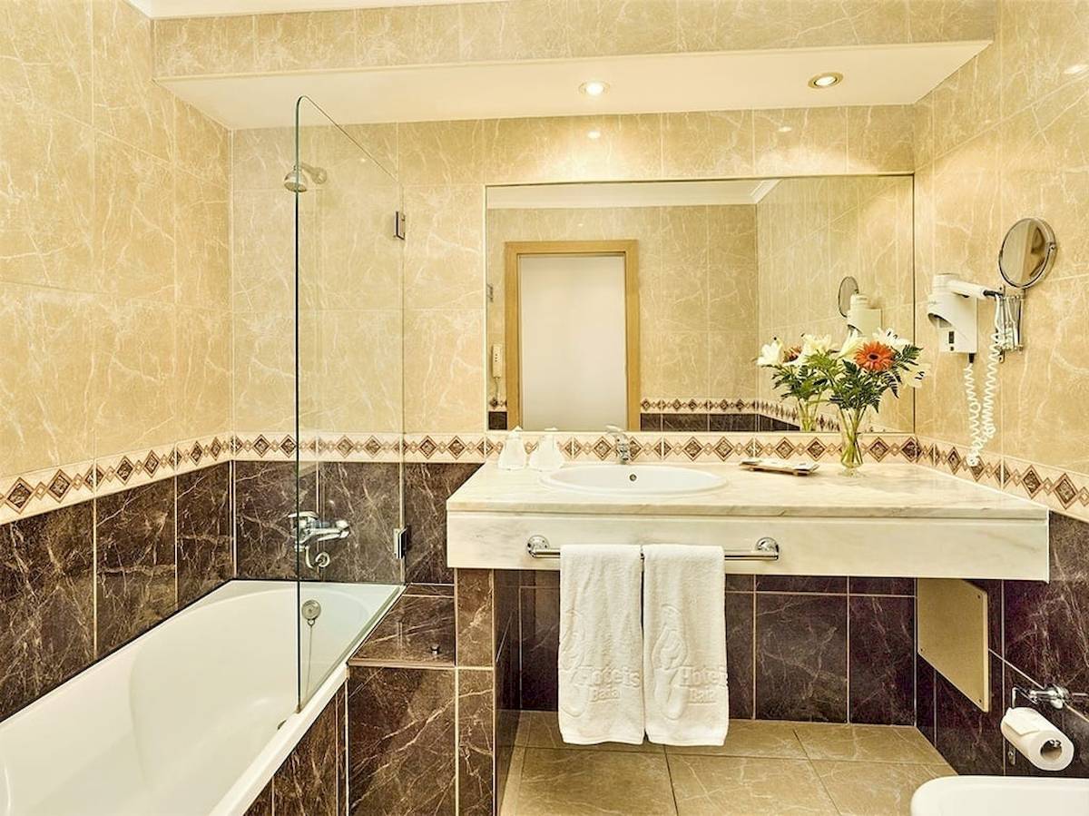 Badezimmer im Baia Grande Hotel mit Badewanne, Waschbecken und Spiegel.
