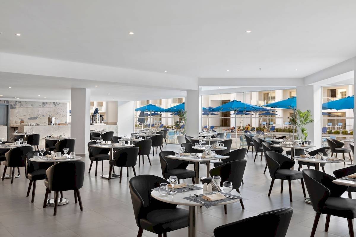 Innenansicht des Restaurants im Pickalbatros Blu Spa Resort mit blauen Sonnenschirmen und Tischen.