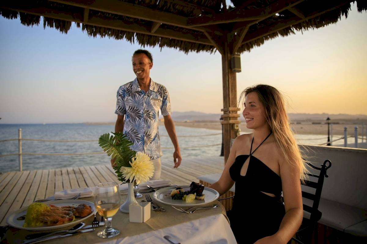 Gast genießt ein Essen auf der Terrasse des Amwaj Beach Club bei Sonnenuntergang.