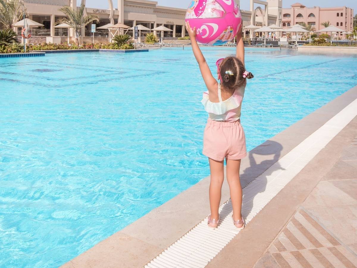 Ein junges Mädchen am Rand des Swimmingpools des Pickalbatros Aqua Vista Resorts, das einen rosa Ball hochhält