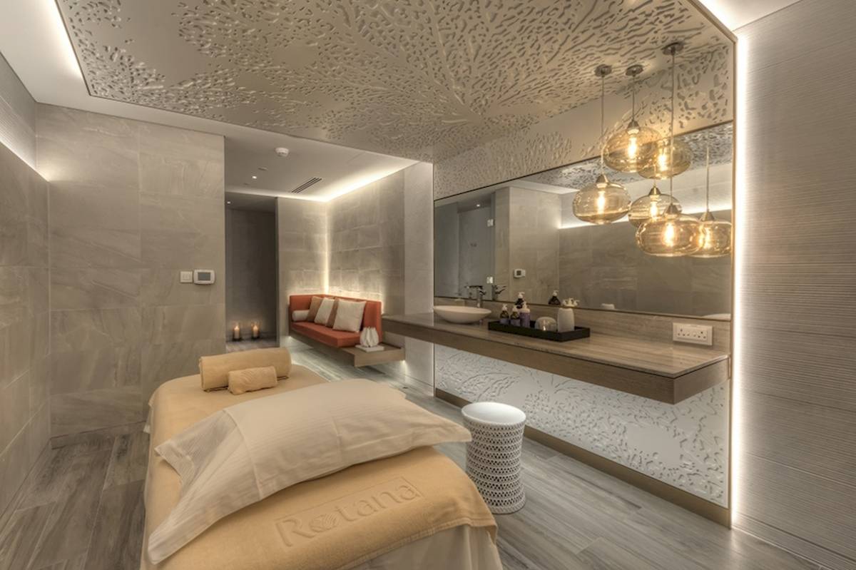 Massagebehandlungsraum im Al Bandar Rotana Hotel mit Liege, Couch, Waschbecken und Spiegel