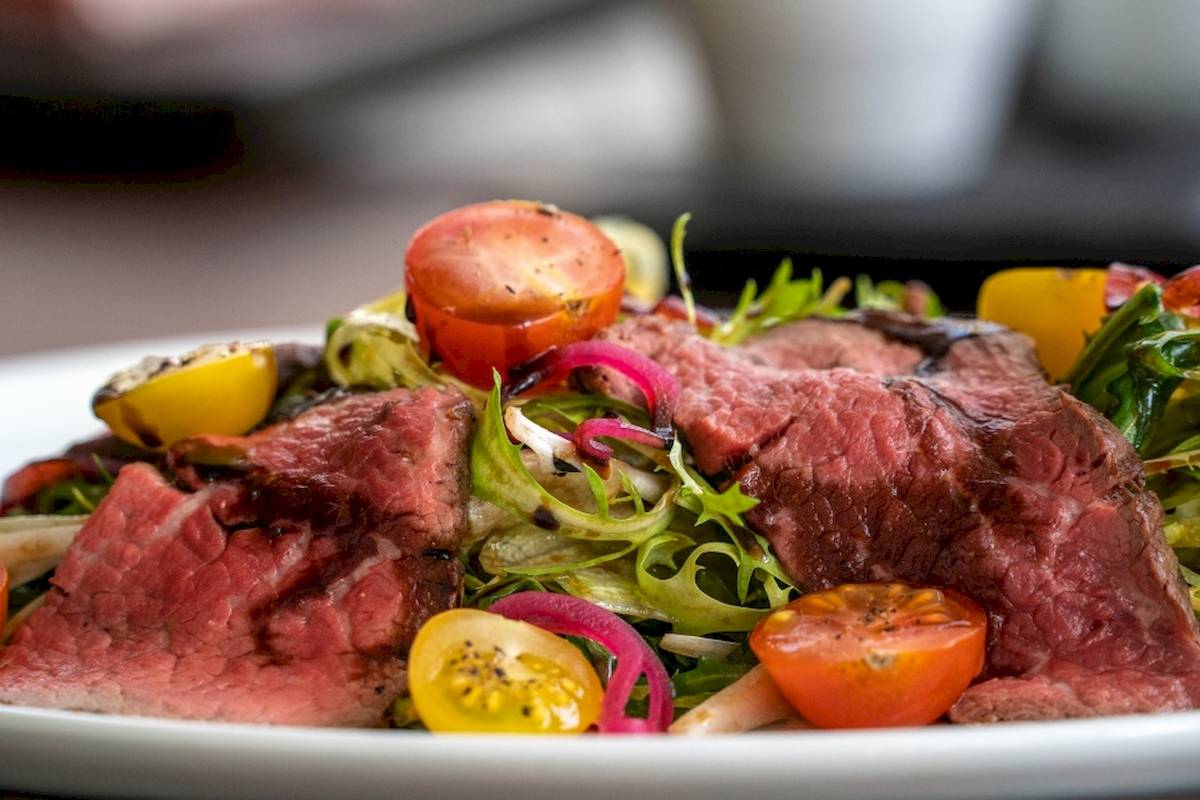 Ein Teller mit einem gegrillten Steak, Salat, Tomaten und Zwiebeln.
