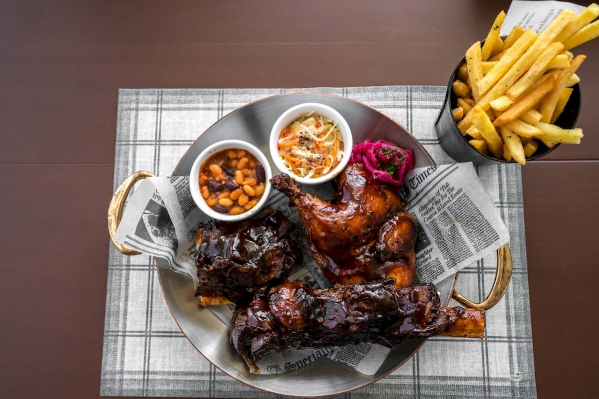 Ein Teller mit gegrilltem Fleisch, Bohnen, Kartoffelstäbchen und einem Salat.