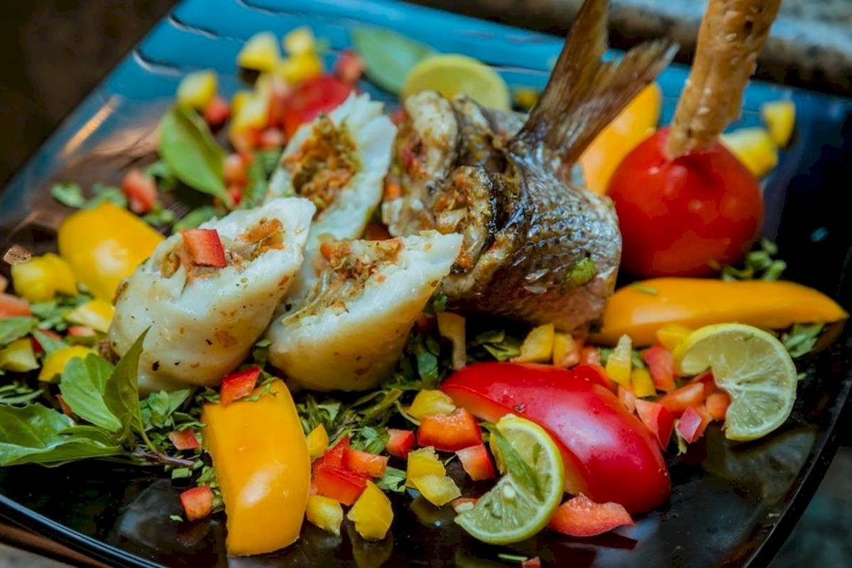 Ein Fischgericht auf einer schwarzen Platte mit verschiedenen Gemüsesorten und Zitronen.