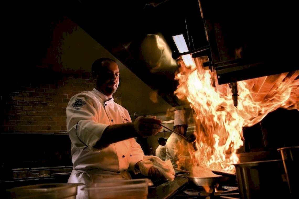 Koch im Restaurant mit brennendem Gericht auf dem Herd