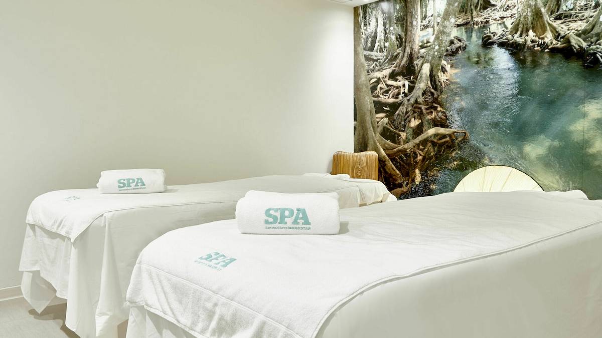 Spa-Behandlungszimmer im Iberostar Cristina Hotel mit weißen Handtüchern und einem Panoramabild an der Wand.