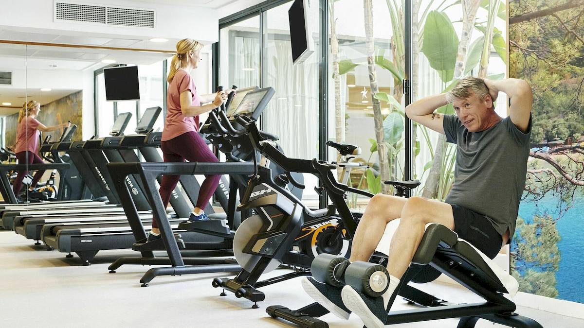 Fitnessstudio im Hotel Iberostar Cristina mit mehreren Personen, die auf Laufbändern und Fahrrädern trainieren.
